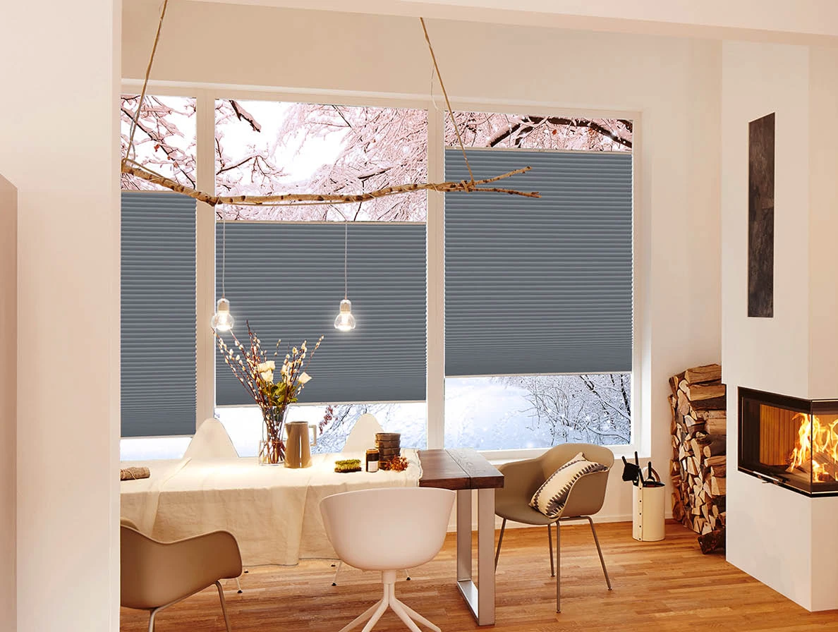 Gemütliches Esszimmer mit grauen Wabenplissees und Kamin im Winter